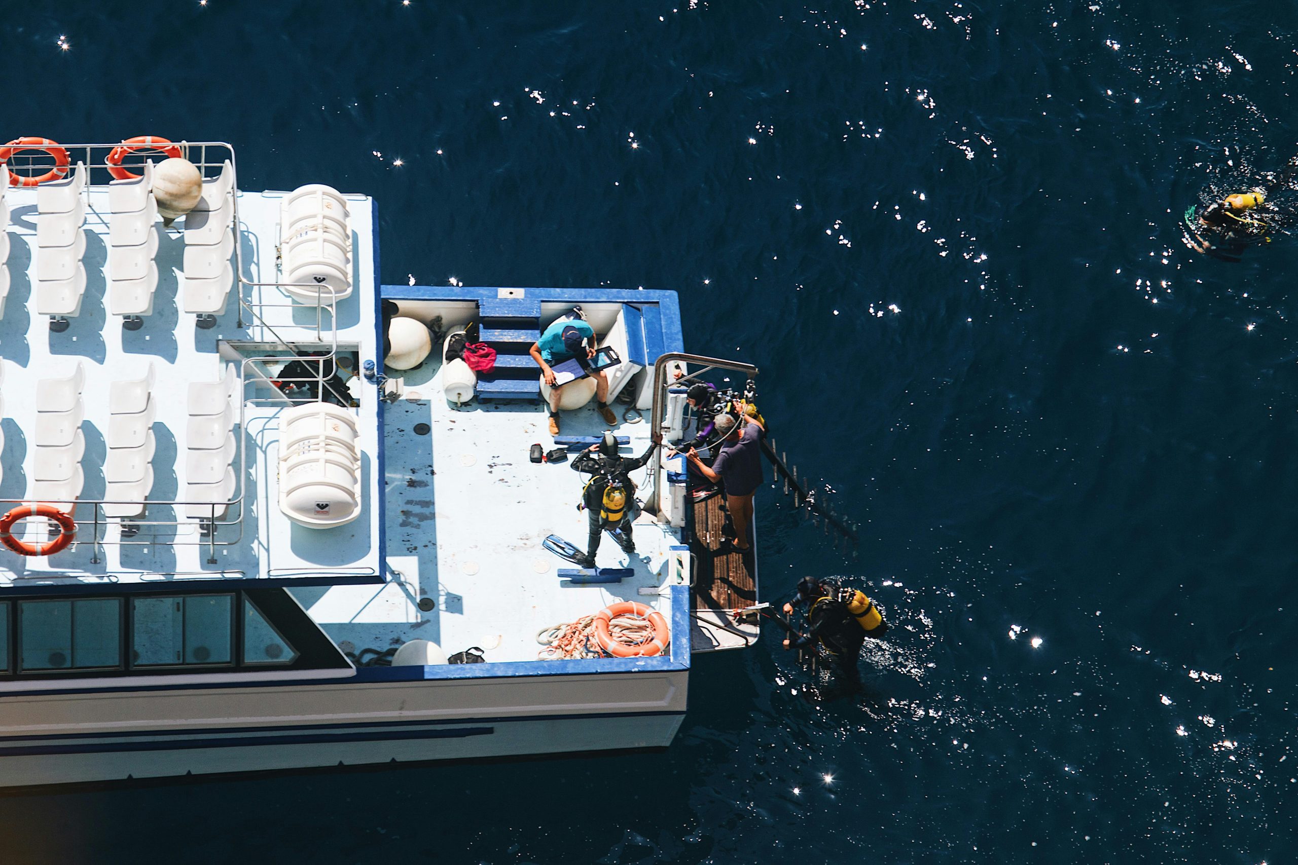 An overhead shot of divers preparing to explore the ocean from a boat under a bright sky.