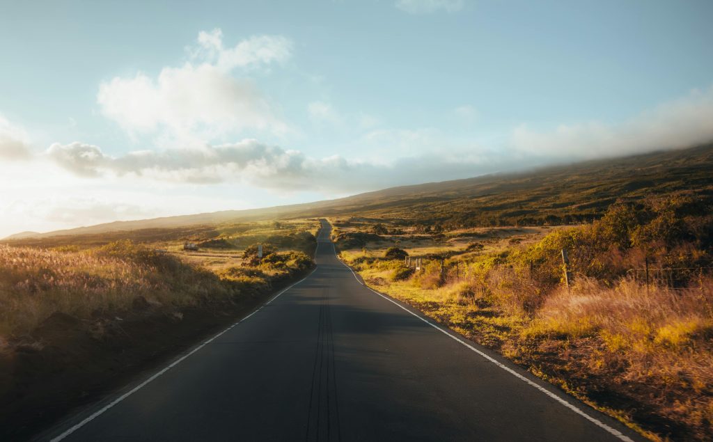 A beautiful road stretching through the Hawaiian landscape at sunrise, showing vibrant colors and dramatic scenery.