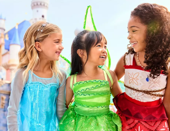 Three young girls looking at one another and smiling while wearing Disney costumes