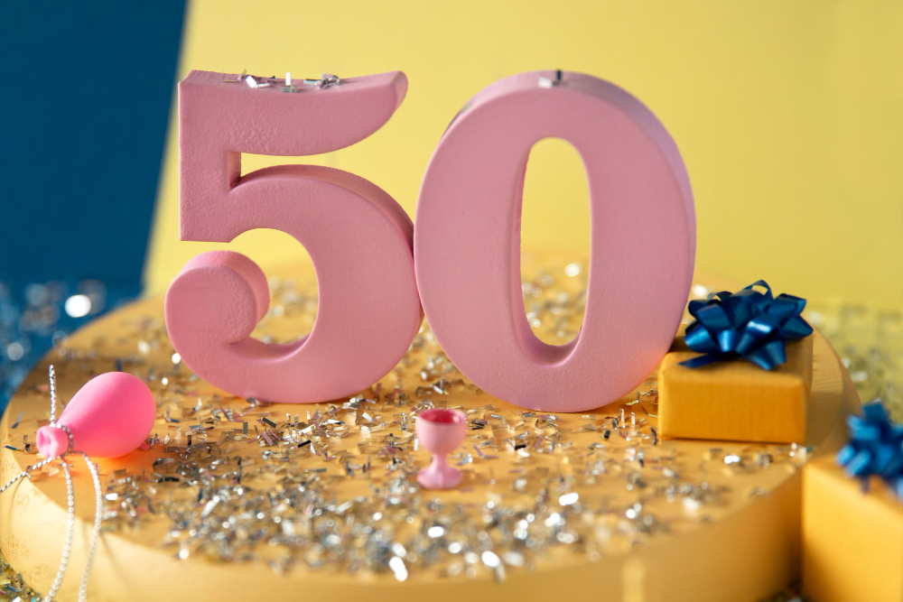 50 in pink 3D letters standing on a yellow platform surrounded by what appears to be silver confetti.