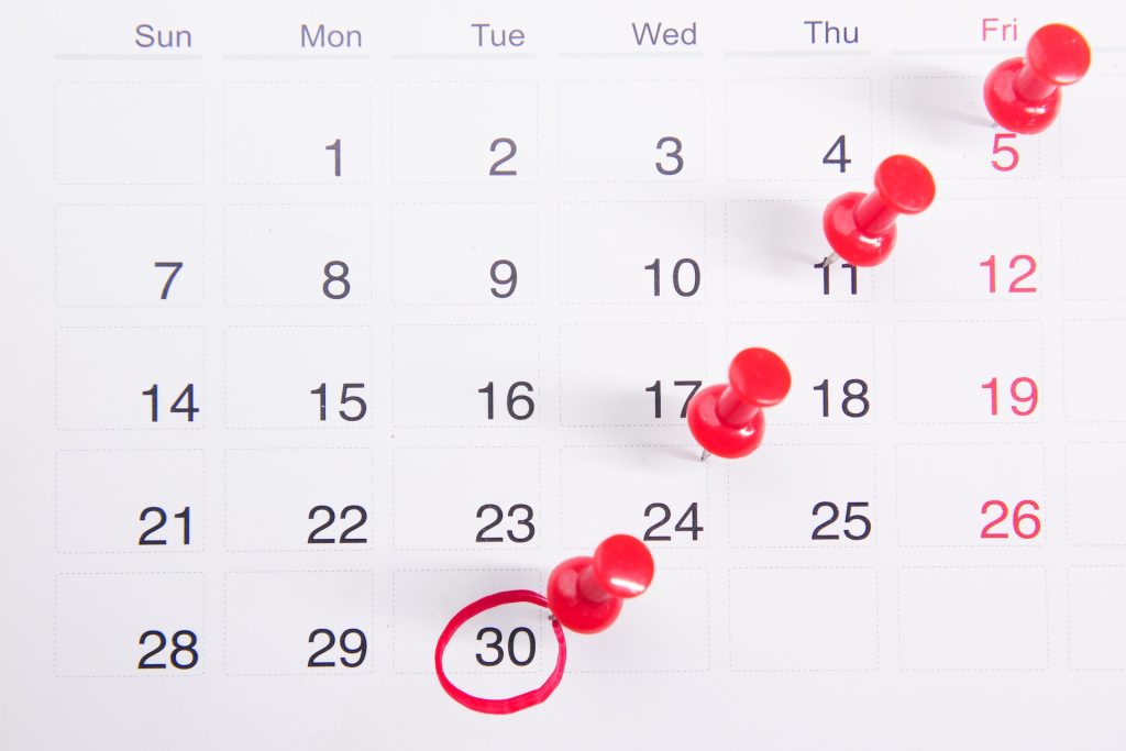 A calendar with red pins sticking into it and the date "30" circled in red.